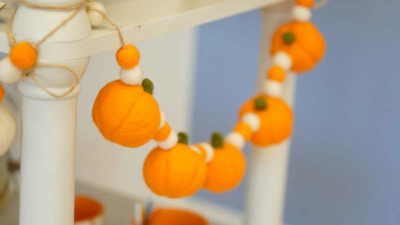 Two hands arranging dried eucalyptus and mini pumpkins on a wooden tray